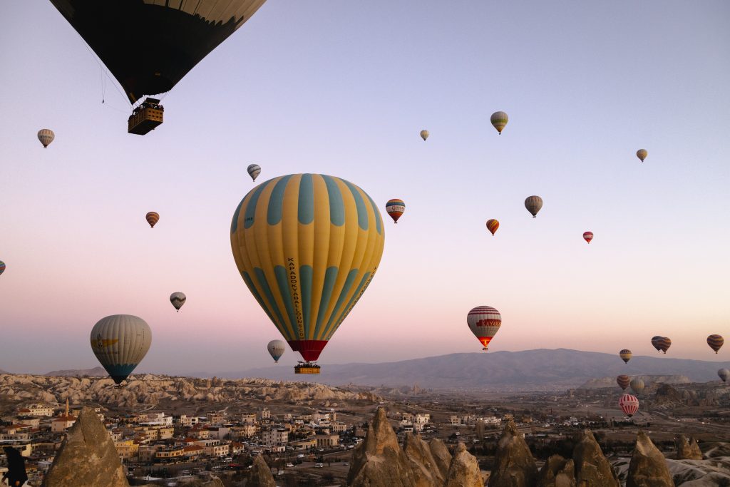 Several colorful hot air balloons rising over a rocky valley and small town at sunrise.