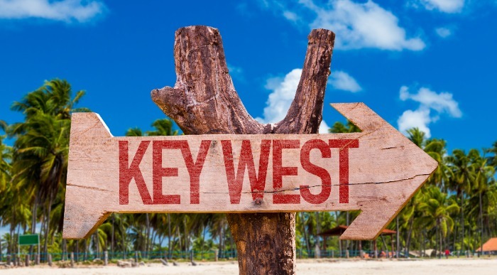 Lesena tabla v obliki puščice stoji na sončni plaži s palmami na Floridi in kaže na Key West