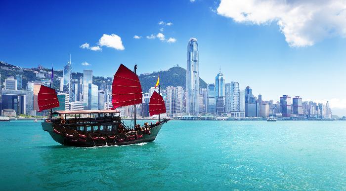 Ladjica pluje po mirnem turkiznem morju pred mestom Hong Kong. 