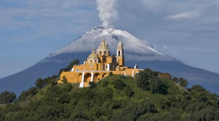 Cerkev na vrhu hriba z vulkanom Popocatepetl v ozadju.