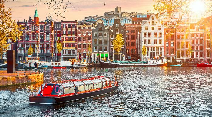 Vožnja z dolgo rdečo ladjico po kanalu v Amsterdamu med pisanimi hišami. 