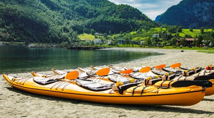 V idilični gorski vasici so ob jezeru pripravljeni oranžno obarvani kajaki. 