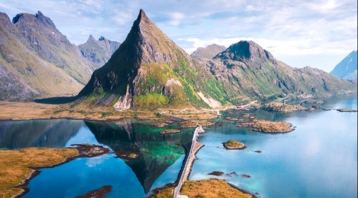 Ozka cesta vodi čez most med fjordi in strmimi gorami v dramatični pokrajini Lofotov na Norveškem