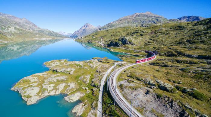 Vlak pelje po vijugasti poti ob ledeniškem jezeru pod gorami. 