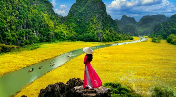 Mlada azijska domačinka opazuje čolne na reki in rumena cvetoča riževa polja.