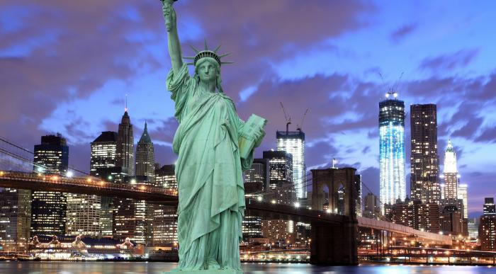 Kip svobode ponoči z osvetljenimi nebotičniki New Yorka v ozadju.